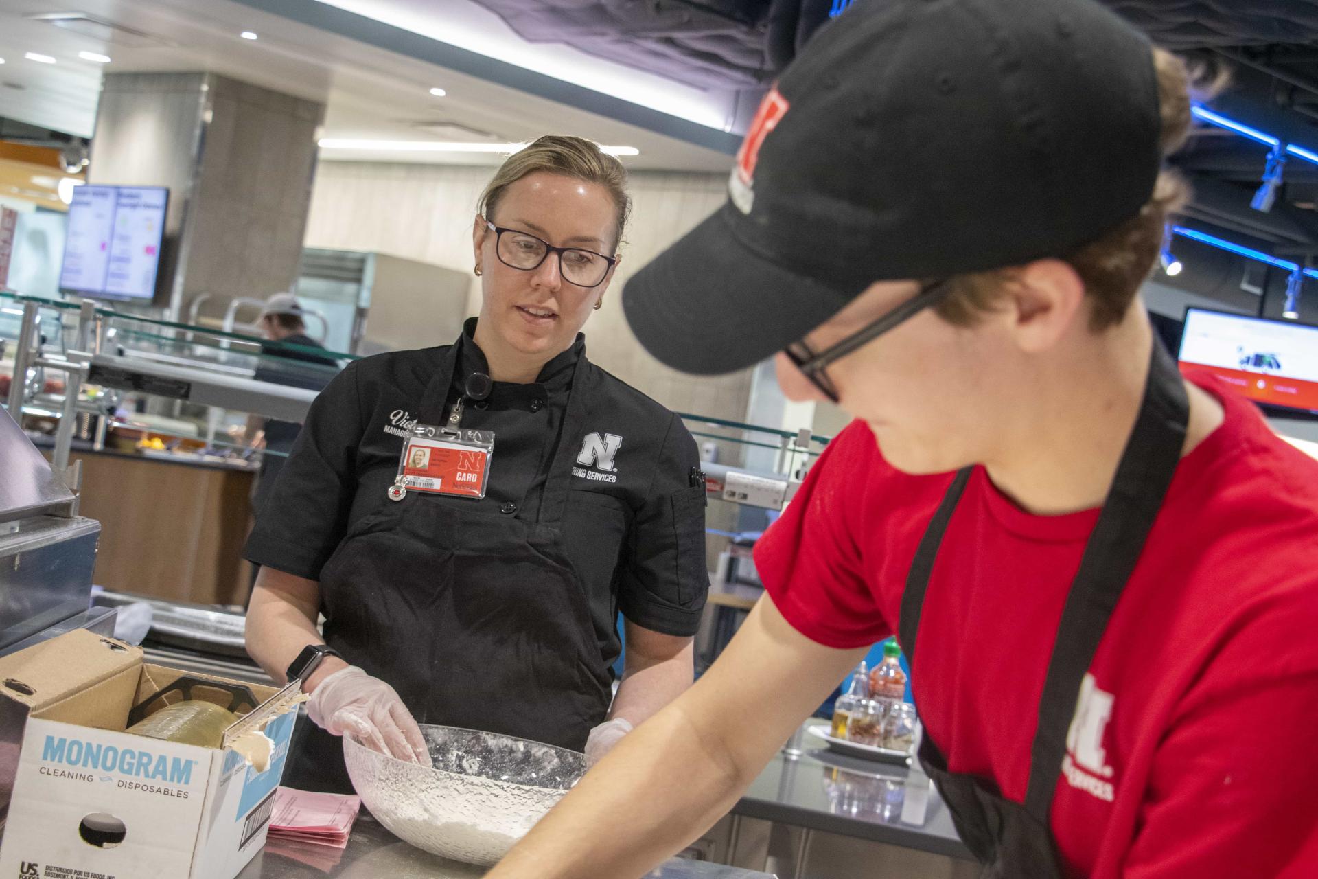Dining staff members overlooks a student staff member preparing menu items