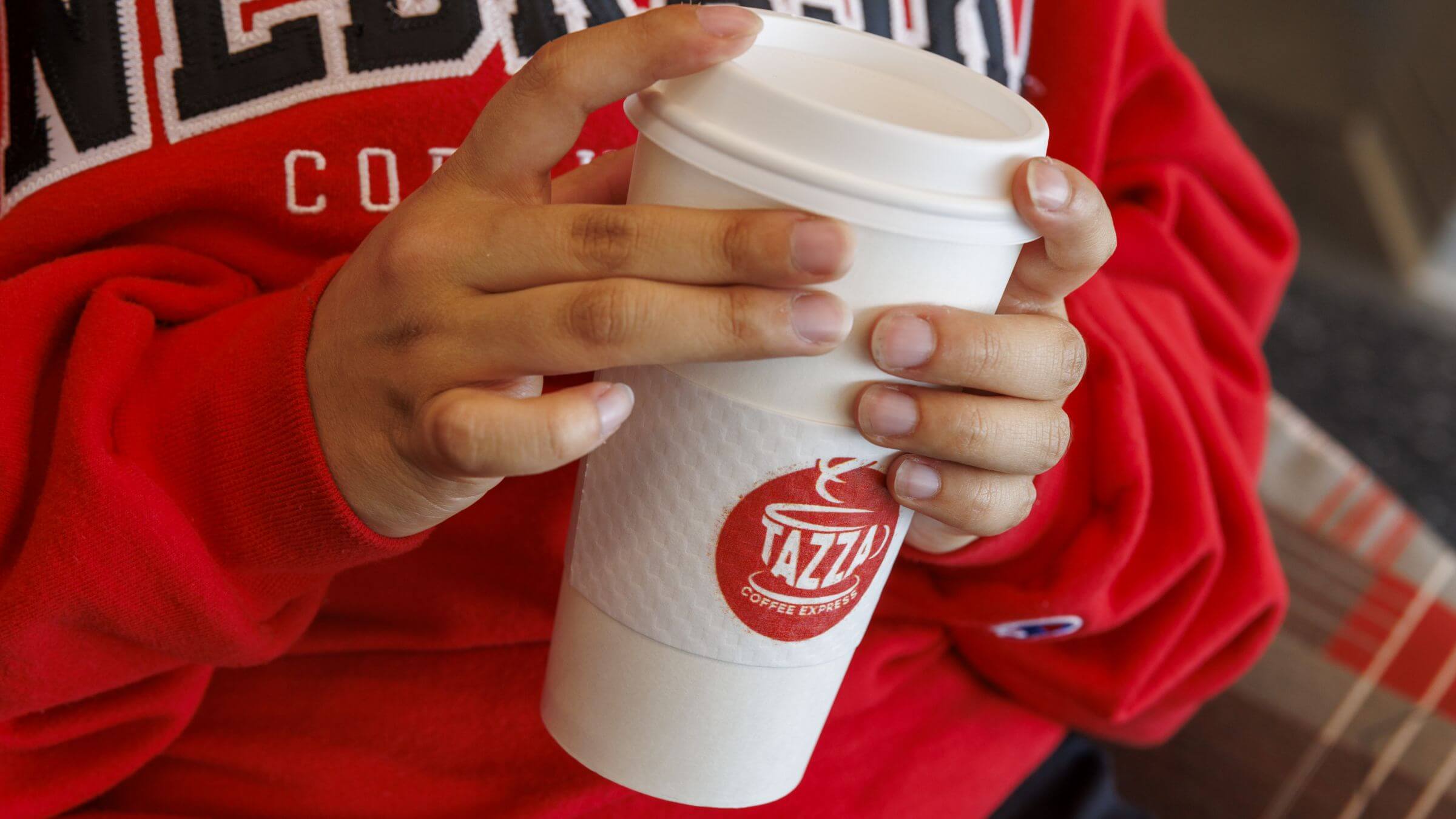 A student holding their Tazza coffee cup.