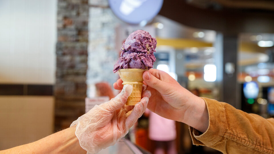 Dining staff member hands a hand dipped gelato cone to a customer
